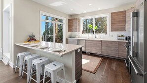 A modern kitchen with a central island, bar stools, and a large refrigerator. - Modern | Beachfront | Sleeps 10 (Oostburg)