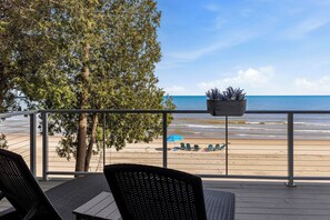 A balcony with wicker chairs, a potted plant, and a view of the beach. - Modern | Beachfront | Sleeps 10 (Oostburg)