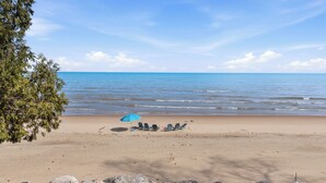 A beach with a row of chairs under a blue umbrella, a rocky foreground, and a clear sky. - Modern | Beachfront | Sleeps 10 (Oostburg)