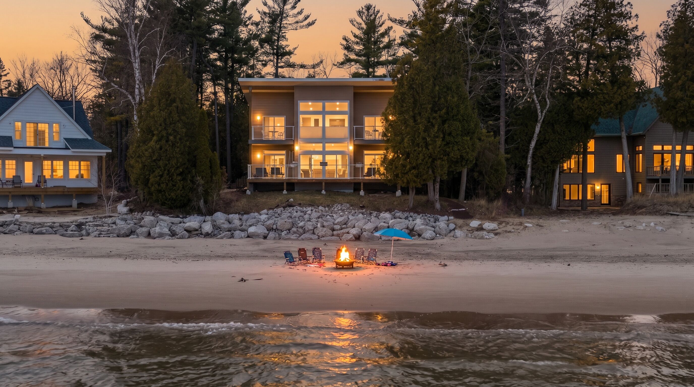 Une propriété située en bord de mer, comprenant un grand bâtiment, un foyer extérieur et une plage de sable.