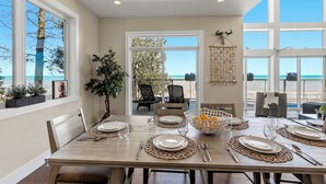A dining area with a view of the ocean, a large window, and a plant. - Modern | Beachfront | Sleeps 10 (Oostburg)