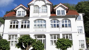 Un bâtiment blanc doté d’une fenêtre centrale en arc de cercle et de plusieurs petites fenêtres, portant l’inscription « Villa Gi ».