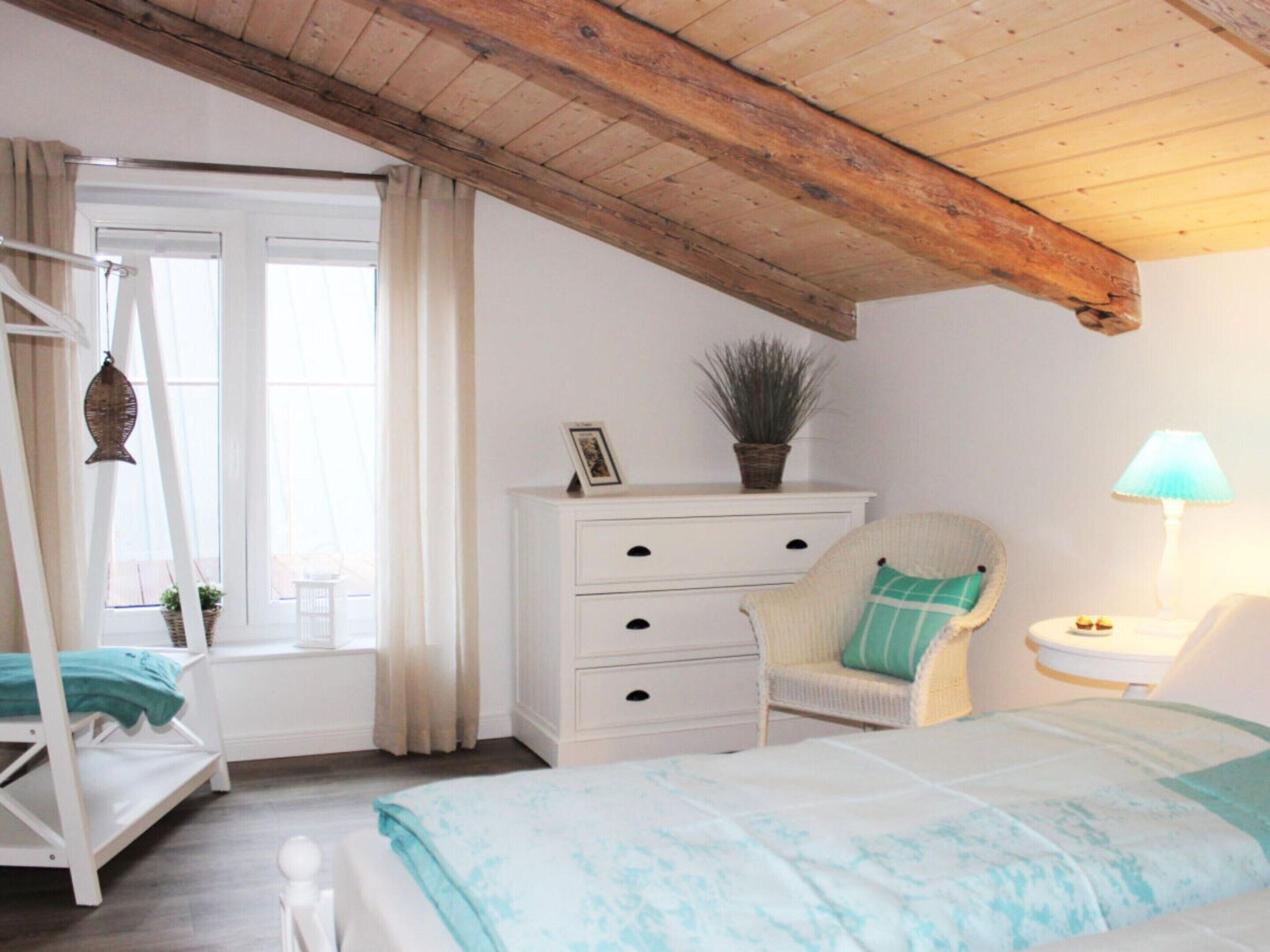 A bedroom with a bed, a chair, a nightstand, a dresser, and a window with curtains.