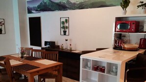 A dining area with wooden tables and chairs, a white cabinet with shelves, and a red microwave on the counter.