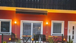 A building with a red facade, multiple windows, and outdoor seating with tables and chairs.