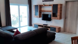 A modern living room with a sofa, TV, and wooden shelving unit.