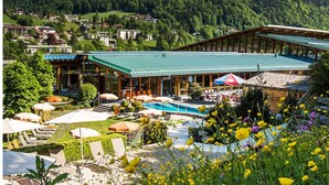 A resort with a swimming pool, outdoor seating, and a mountain backdrop.