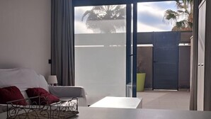 A modern living room with a sofa, a coffee table, and a view of a gated outdoor area with palm trees. - Belvilla by OYO Apartamento con Patio (Fuengirola)