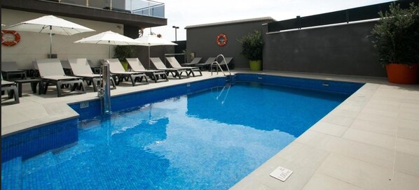 A swimming pool with lounge chairs and umbrellas, surrounded by a tiled deck.