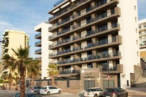 A multi-story residential building with balconies, a gated entrance, and parked cars.