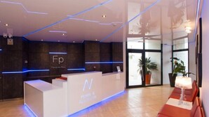 A modern hotel reception area with a white reception desk, a seating area with red chairs, and a glass wall offering a view of indoor plants. - Belvilla by OYO Apartamento con Patio (Fuengirola)