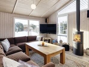 Ett mysigt vardagsrum med ett träpanelat tak, ett stort fönster, en platt-TV, ett träbord och en vedkamin.