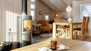 A cozy room with a wood-burning stove, a dining table with chairs, and a window providing natural light.