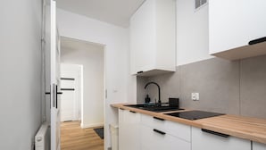 A modern kitchen with white cabinets, a wooden countertop, and a black faucet. - Ochota Comfort Apartment (Warszawa)