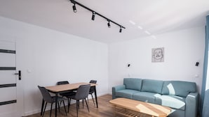 A modern living room with a wooden dining table, black chairs, a blue sofa, and a wooden coffee table. - Ochota Comfort Apartment (Warszawa)