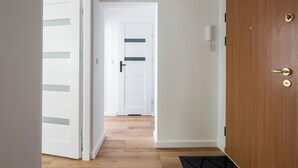 A hallway with wooden flooring, white walls, and a wooden door with a brass handle. - Ochota Comfort Apartment (Warszawa)