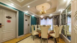 A dining area with a round table and six chairs, a chandelier, and a view through large windows.