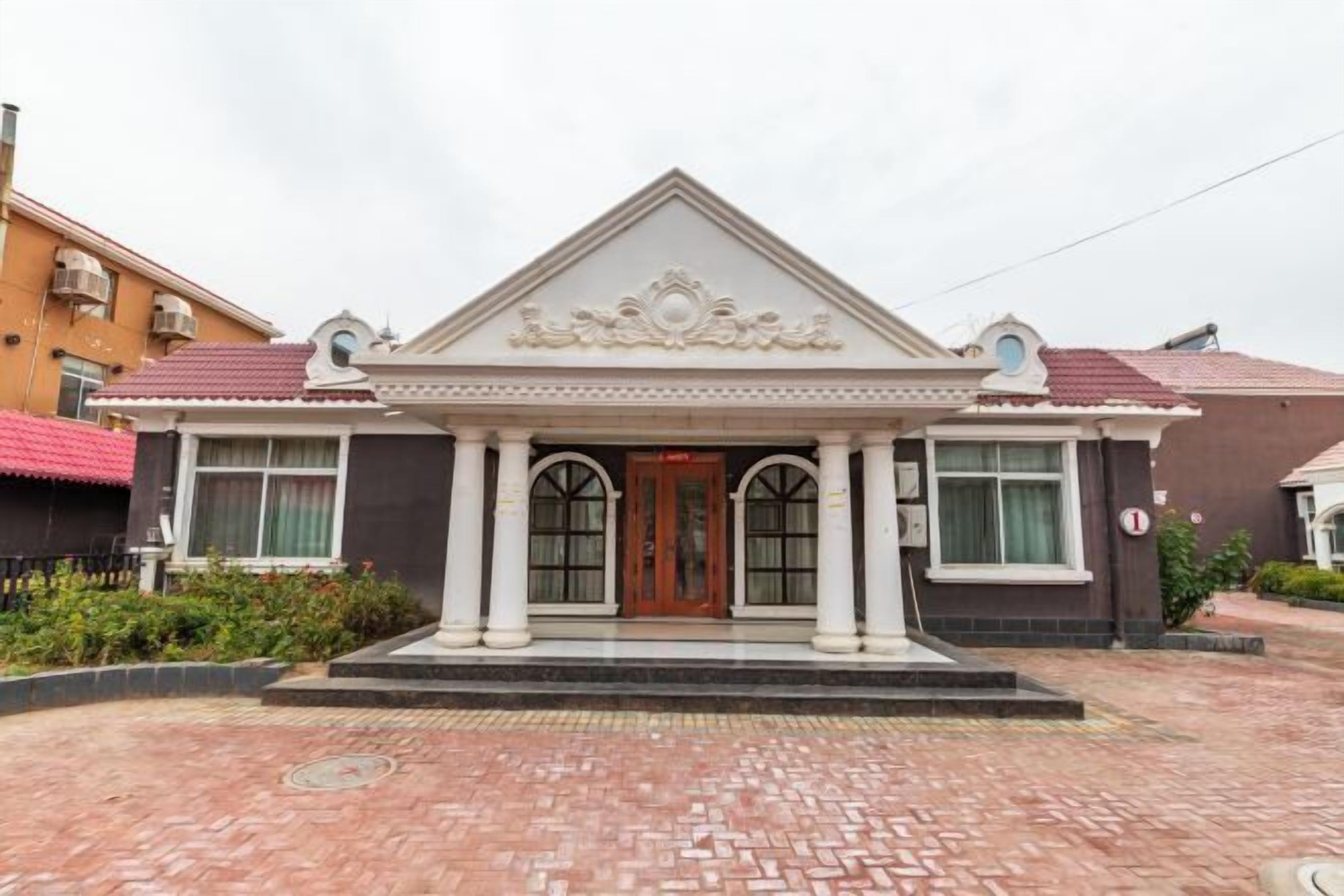 A building with a symmetrical facade, a central entrance with a decorative pediment, and a brick-paved entrance area.