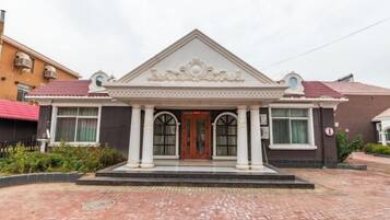 A building with a symmetrical facade, a central entrance with a decorative pediment, and a brick-paved entrance area.