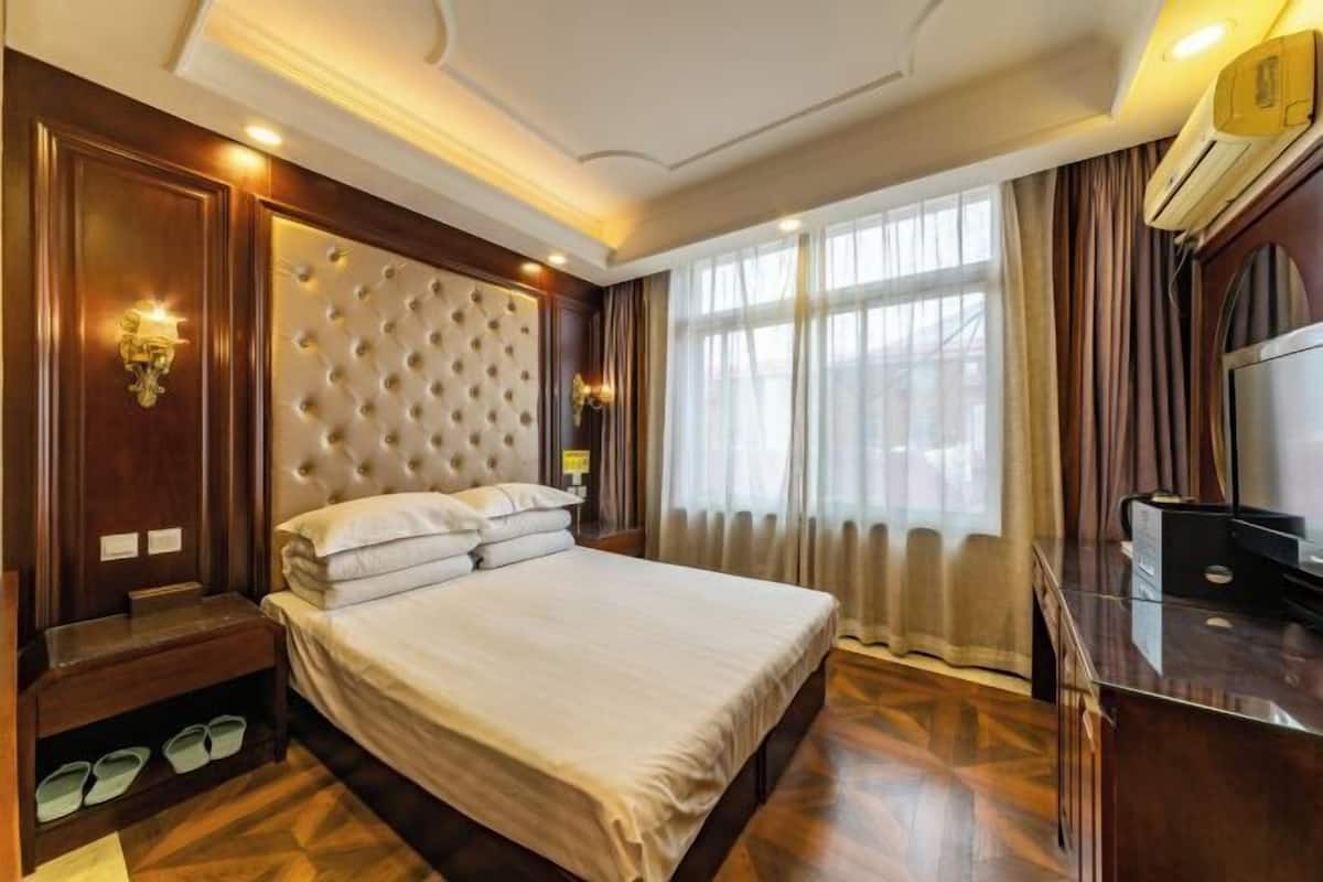 Habitación de hotel con una cama grande, paneles de madera, televisor y ventana con cortinas.