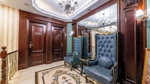 A grand hallway with a marble floor, ornate wooden doors, and blue upholstered chairs.