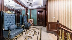 A grand hallway with ornate blue armchairs, a chandelier, and a patterned rug.