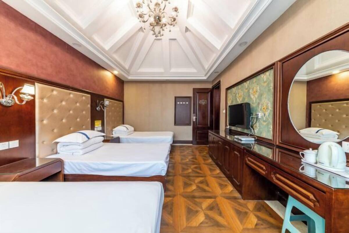 Habitación de hotel con dos camas, un espejo grande, un televisor y piso de madera.