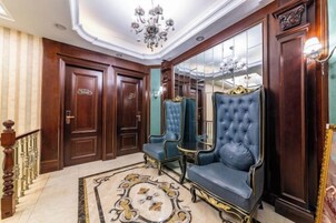 Un lobby espacioso con candelabro, paneles de madera ornamentados y un sillón tapizado en azul.