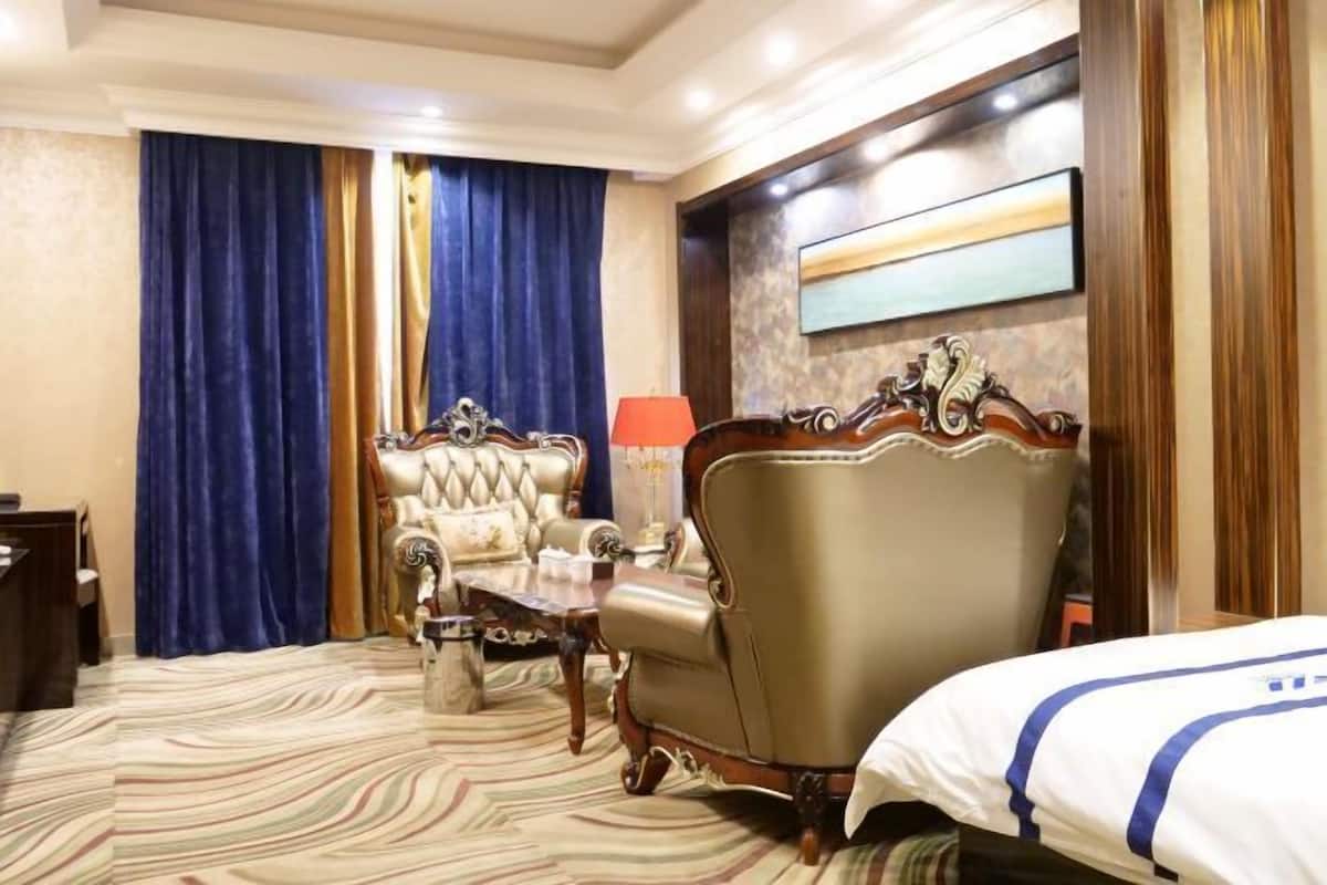 Una habitación de hotel con una cama grande, un sillón, una mesita y una lámpara.