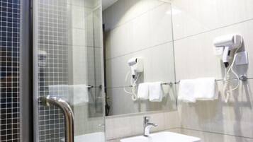 A modern bathroom with a glass shower enclosure, a white sink, and two hair dryers mounted on the wall.