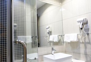 Un baño moderno con cabina de ducha de vidrio, un lavamanos blanco y dos secadores de pelo fijados a la pared.