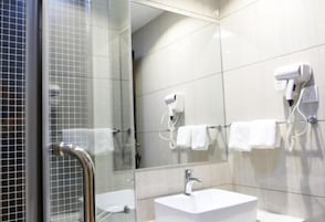Un baño moderno con cabina de ducha de vidrio, un lavamanos blanco y dos secadores de pelo fijados a la pared.