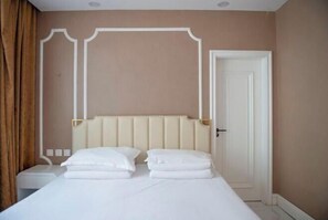 Habitación de hotel con cama, mesita de noche, puerta y pared con molduras decorativas.