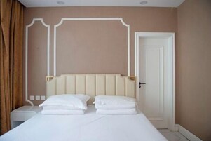 Habitación de hotel con cama, mesita de noche, puerta y pared con molduras decorativas.