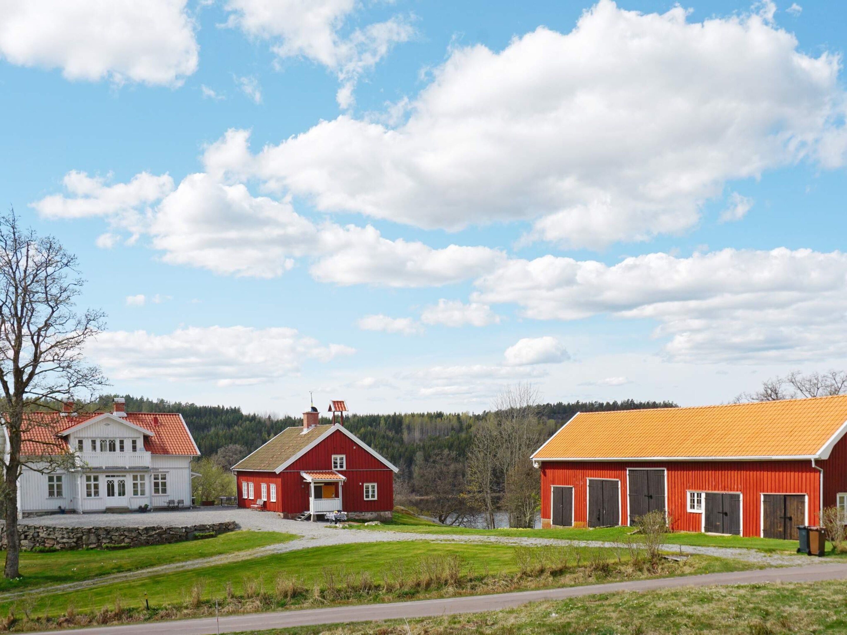 Ett lantligt landskap med ett vitt hus, en röd lada och en byggnad med ett gult tak.