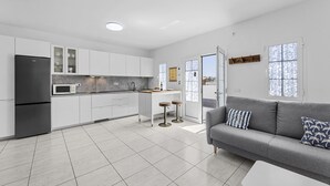 A modern kitchen with white cabinets, a black refrigerator, and a microwave. There is a grey sofa with patterned cushions and a white coffee table. - "Oasis" Apartment in Playa Blanca | Lanzarote - Spain (Playa Blanca)