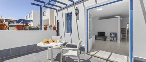 Eine Terrasse mit Tisch und Stühlen, Kübelpflanzen und einer pergolaartigen Struktur mit blauen Rahmen.