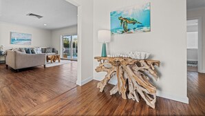 Un salón espacioso con suelo de madera, un sofá gris, una mesa de centro de madera y un cuadro de una tortuga marina.
