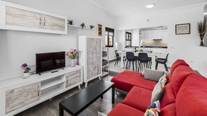 A modern living room with a red sofa, a TV, and a dining area with chairs and a table. - Casa Nadal | Holiday Home in Playa Honda - Lanzarote (Playa Honda)