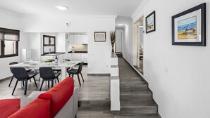 A modern kitchen with white cabinets, a dining area with a red sofa, and a staircase leading to another level. - Casa Nadal | Holiday Home in Playa Honda - Lanzarote (Playa Honda)