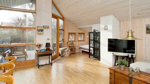 A spacious room with a large window, wooden flooring, a bed, a TV, and a bookshelf. - 6 Person Holiday Home in Nykobing Sj (Nykobing Sjaelland)
