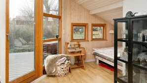 A cozy room with wooden walls, a large window, a bed, a chair, a small table, and a cabinet with glass doors. - 6 Person Holiday Home in Nykobing Sj (Nykobing Sjaelland)