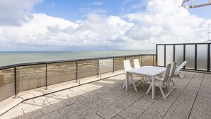 Une terrasse avec une table et des chaises, donnant sur une plage et la mer.