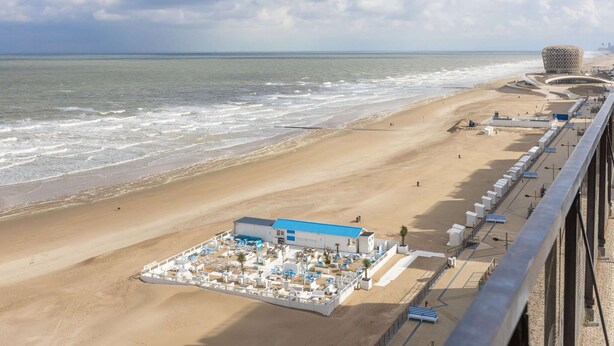 Un hôtel situé en bord de mer, doté d’une piscine entourée d’une clôture, d’un accès direct à la plage et d’un bâtiment à l’architecture remarquable en arrière-plan.