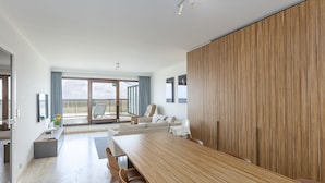 Une chambre d’hôtel moderne dotée d’une grande table à manger en bois, de sièges confortables, d’un balcon avec vue et d’une porte-fenêtre coulissante.