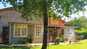 Un bâtiment en pierre doté de grandes fenêtres et d’un toit recouvert de tuiles, entouré d’une pelouse bien entretenue et de plantes en pot.
