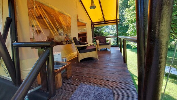 Un espace extérieur aménagé, abrité et doté de chaises en osier et d’une terrasse en bois, offrant une vue sur un jardin luxuriant.
