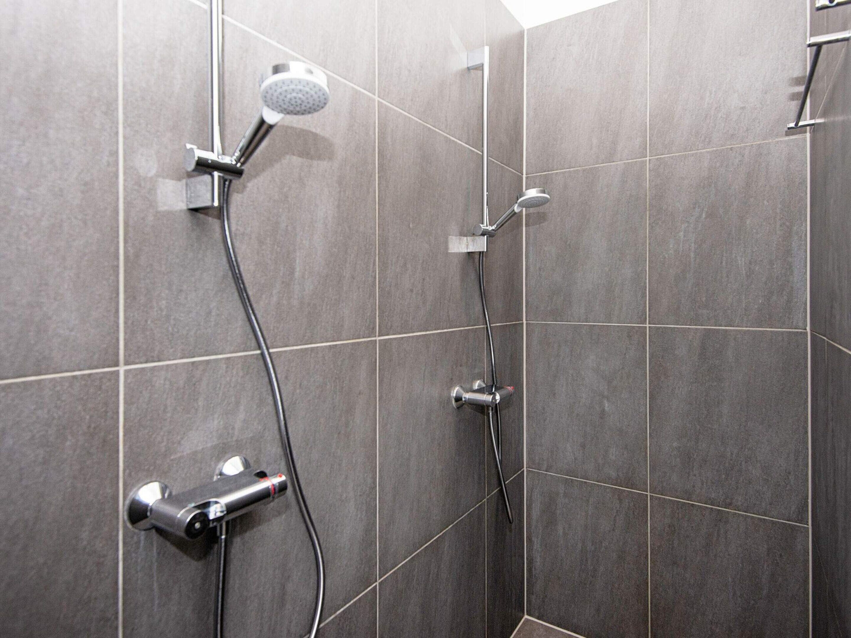 A shower area with a handheld showerhead, a wall-mounted faucet, and a handheld shower attachment.