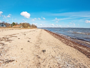 Ein Strand mit sandigem Ufer, vereinzelten Felsen und blauem Himmel.