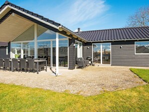 Ein modernes Haus mit überdachter Terrasse, Sitzgelegenheiten im Freien und einer großen Glasdoor, die auf eine Terrasse führt.